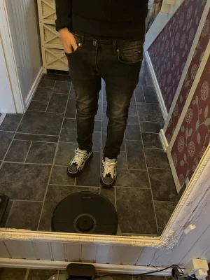 Svarta slim fit jeans med slitningar - Säljer ett par svarta slim fit jeans med snygga slitningar och tvättade detaljer på låren. Klassisk femficksmodell med knapp och dragkedja. Jeansen har en modern passform som sitter tight över benen och passar perfekt till sneakers.