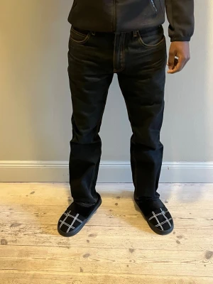 Cheap Monday Jeans - Svarta jeans från ”Cheap Monday” med orange kontrastsömmar och unik dödskalle-patch bak i midjan. Innerfoder med tryckta dödskallar i ljusgrönt. Klassisk femficksmodell med rak passform och dragkedja. Perfekt för dig som vill sticka ut med coola detaljer.. Materialet är denim i bomull.