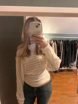 Vit offshoulder topp med ballongärm - Trendig vit offshoulder topp med långa ballongärmar och smockad midja. Tunt, lätt material med diskreta ränder som ger en snygg struktur. Perfekt för dig som vill ha en luftig och stilren look.