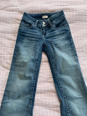 Blå bootcut jeans med rosa broderi - Säljer ett par blå bootcut jeans från Nelly med snyggt rosa broderi på bakfickorna. Jeansen har klassisk femficksmodell, normalhög midja. Perfekta till vardagsstilen och passar till det mesta! Byxorna är från Nelly i storlek 32. Jeansen har även en liten fläck under ena fickan men det är inget man tänker på. 