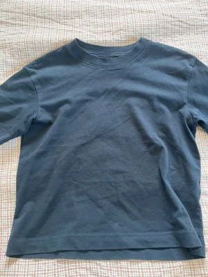Mörkblå basic t-shirt i bomull - En enkel och stilren mörkblå t-shirt i mjuk bomull. T-shirten har rund halsringning och korta ärmar, perfekt för en avslappnad look. Passformen är normal och materialet känns skönt mot huden. Från Gina Tricot och är aldrig använd. I storleken xxs. 