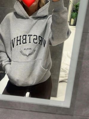 Grå hoodie WRSTBHVR Berlin - Säljer en grå hoodie från WRSTBHVR med svart text 'WRSTBHVR Berlin' och en liten lagerkrans på bröstet. Hoodien har stor huva, magficka och ribbade muddar. Perfekt oversized fit och mjukt material, troligen bomullsmix.