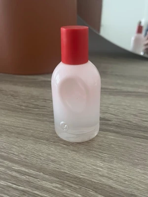 Glossier You Eau de Parfum 50ml - Glossier You Eau de Parfum i en stilren, matt ljusrosa glasflaska med röd kork. Flaskan har en unik, rundad form och är tillverkad i glas. Parfymen är känd för sin fräscha och personliga doft som anpassar sig efter bäraren.