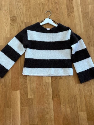 Randig stickad tröja Gina Tricot - Stickad tröja från Gina Tricot med breda svarta och vita ränder. Tröjan har rund halsringning och långa ärmar. Perfekt för dig som gillar en enkel men trendig look med lite oversized känsla.