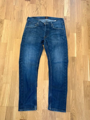Mörkblå jeans från Lee - Snygga mörkblå jeans från Lee med klassisk femficksdesign och raka ben. Jeansen har en lätt tvättad look och Lee-logga på bakfickan. Perfekta för en avslappnad stil och tillverkade i bomull för skön komfort.