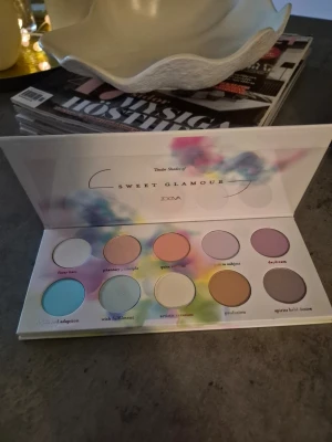 Zoeva Sweet Glamour ögonskuggspalett - Säljer en Zoeva Sweet Glamour ögonskuggspalett med 10 färger i pastelltoner som blått, rosa, lila, beige och gult. Paletten har rund form på skuggorna och ett färgglatt, konstnärligt fodral. Perfekt för dig som gillar kreativa och färgstarka looks. Kan vara testad,swatchad.