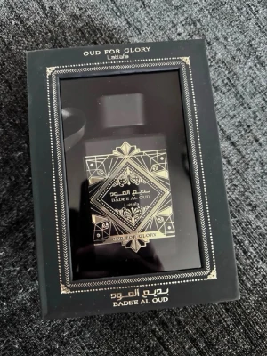 Lattafa Badee Al Oud Oud For Glory - Lyxig parfym från Lattafa i en svart, fyrkantig flaska med elegant gulddetaljer och orientaliskt mönster. Flaskan kommer i en exklusiv svart förpackning med fönster och guldtext. Doften heter Badee Al Oud Oud For Glory och utstrålar mystik och elegans.