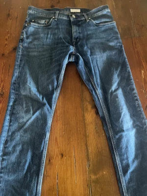 Blå  jeans från Tiger of Sweden  - Säljer ett par blå jeans från tiger of Sweden  med klassisk femficksmodell och snygga slitningar. Jeansen har normal midja, dragkedjegylf och är tillverkade i bomull med lite stretch för skön passform. Perfekta till en avslappnad stil.
