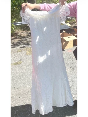 Vit lång spetsklänning offshoulder - Romantisk vit långklänning med vacker spets och offshoulder-design. Klänningen har en figurnära passform och fina spetsdetaljer längs axlarna. Perfekt för sommarens speciella tillfällen.    Endast använd vid vigsel. 