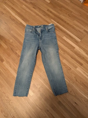 Levis stl 26  - Säljer ett par ljusblå jeans med rak passform och rå, avklippt kant nertill. Jeansen har klassisk femficksdesign och dragkedjegylf. Perfekta för en avslappnad och trendig look.Mile High Super Skinny.Observera avklippta nertill
