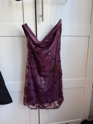 Lila blommig miniklänning från Peppermayo - Superfin lila kortklänning från Peppermayo utan axelband och blommigt mönster med paljettdetaljer. Helt ny med prislapp kvar, nypris 108,95€
