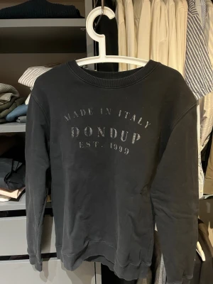 Svart sweatshirt från Dondup - Cool svart sweatshirt från Dondup med tryck på bröstet där det står 'Made in Italy Dondup Est. 1999'. Tröjan har rund halsringning, ribbade muddar vid ärmslut och nederkant. Perfekt till en avslappnad stil.