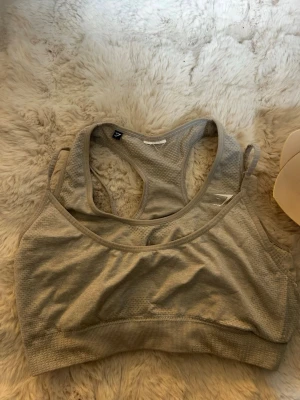Grå sport-bh från Gymshark - Säljer en grå sport-bh från Gymshark med brottarrygg och ventilerande meshdetaljer. Bh:n har en bred resår under bysten för extra stöd och är tillverkad i ett stretchigt funktionsmaterial. Perfekt för träning eller en aktiv vardag. Står ej storlek men skulle gissa på S. Ilägg medföljes