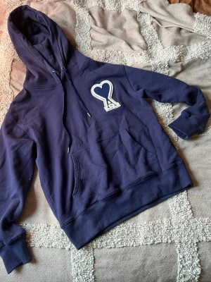 Mörkblå hoodie från AMI Paris - Snygg mörkblå hoodie från AMI Paris med vit broderad hjärtlogga på bröstet. Klassisk känguruficka, ribbade muddar och dragsko i huvan. Perfekt för en chill och trendig look. Mjuk bomullskvalitet. Pris kan diskuteras vid snabb affär