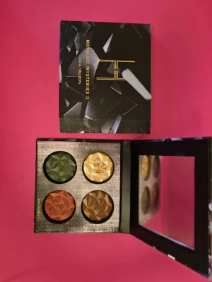 LH Cosmetics Metallic Mysteries II - Snygg ögonskuggspalett från LH Cosmetics med fyra metalliska nyanser: djupgrön, guld, koppar och brons. Skuggorna har en unik, facetterad yta och kommer i en stilren svart ask med spegel i locket. Perfekt för dig som älskar intensiva färger och metallic-finish. 1-2  skuggor är swathade en gång. 