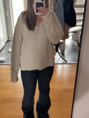 Beige stickad tröja från H&M - Mysig beige stickad tröja från H&M med v-ringning och avslappnad passform. Tröjan har långa ärmar och ribbade muddar vid ärmslut och nederkant. Perfekt för lager på lager och enkel att matcha till olika outfits.
