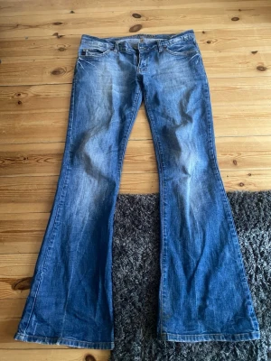 Blå bootcut jeans med slitningar - Snygga blå bootcut jeans med lätt slitna detaljer och klassisk femficksdesign. Jeansen har utsvängda ben och detaljer på fickorna. Endast använda fåtal gånger så fint skick! Midjemått 80 cm innerben 77 Ytterben 97