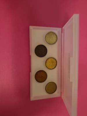 Ögonskuggspalett från Pat McGrath - Snygg ögonskuggspalett med fem skimrande nyanser i grönt, guld, brons och brunt. Paletten kommer i ett stilrent vitt plastfodral med genomskinligt lock och guldiga detaljer. Perfekt för att skapa kreativa och färgstarka ögonlooker. Tror den är helt oanvänd. Men säger kanske swatchad  någon skugga . En fin palett. 