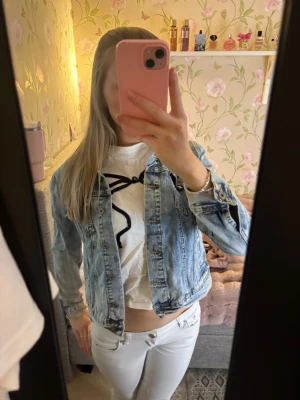 Ljusblå klassisk jeansjacka - Snygg ljusblå jeansjacka med klassisk passform och knappar framtill. Jackan har två bröstfickor med lock och knapp, samt sömmar som ger en cool vintagekänsla. Perfekt att slänga över en t-shirt för en avslappnad look. Den sitter som en S/M.