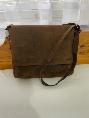 Brun datorväska i läder från LEABAGS - Rymlig läderväska från Leabags. Klassisk messenger modell i äkta läder med en snygg vintagekänsla. Lädret åldras fint och får en ännu snyggare karaktär med tiden och användning.  Väskan har flera praktiska fack och ett rymligt huvudfack som passar perfekt för dator, böcker eller dokument. Justerbar axelrem gör den bekväm att bära till arbete, studier eller vardag.