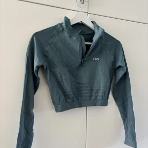 Grön croppad träningstopp från ICANIWILL - Sportig  croppad topp från ICANIWILL med lång ärm och half zip framtill. Tillverkad i stretchigt syntetmaterial som andas, perfekt för träning. Diskret logga på bröstet och ribbade detaljer vid midjan för extra komfort. Passar nog även S, använd 1 gång