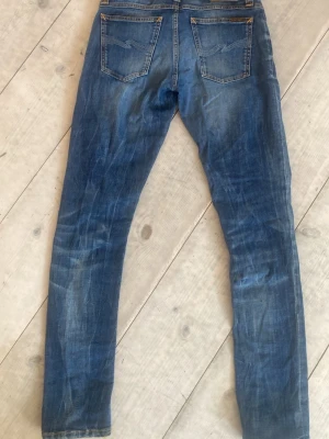 Blå slim fit jeans från Nudie Jeans - Säljer ett par klassiska blå slim fit jeans från Nudie Jeans., snygga slitningar och kontrastsömmar. Tillverkade i bomull med en skön stretch. Perfekta för dig som gillar en smal passform och tidlös stil. Kan diskutera pris 