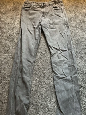 Grå kappahl jeans - Säljer ett par grå jeans med rak passform och klassisk femficksdesign. Jeansen har bälteshällor, knappgylf och är tillverkade i ett mjukt denimtyg. Perfekta för en avslappnad och stilren look.
