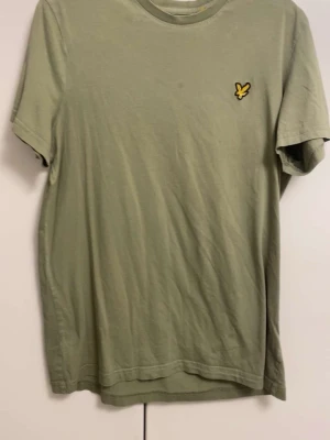 Grön t-shirt från Lyle & Scott - Snygg grön t-shirt från Lyle & Scott med klassisk gul logga på bröstet. T-shirten har rund halsringning och korta ärmar. Perfekt basplagg till garderoben och enkel att matcha med olika stilar.