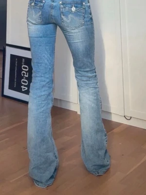 Ljusblå bootcut jeans med fickdetaljer - Säljer ett par ljusblå bootcut jeans som är helt slutsålda,med snygga fickdetaljer bak och klassisk femficksdesign. Jeansen har låg midja och är tillverkade i denim med lätt tvättad look. Perfekta för dig som gillar retrostil och vill ha ett par jeans som sticker ut. Jeansen är lite uppsydda för att pass mig men är enkelt att sprätta upp! 