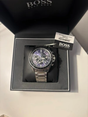 Silverfärgad klocka från Hugo Boss - Stilren klocka från Hugo Boss med silverfärgad länkarmband och svart urtavla med flera små urtavlor. Klassisk design med tydliga markeringar och robust metallarmband. Perfekt accessoar för dig som gillar en elegant och modern look. ENDAST SERIÖS BUD KLOCKAN SKICKAS INOM EN DAG! Skriv för mer info privat!