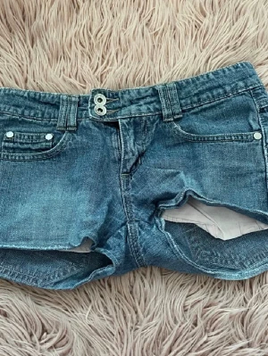 Blå Low waist jeansshorts  - Snygga blå jeansshorts med dubbla knappar i midjan och klassiska fem fickor. Shortsen har bälteshällor och är tillverkade i ett slitstarkt denimtyg. Perfekta för varma dagar och ger en avslappnad look.