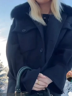 Meotine Jacka S/M - Stilren svart jacka från Meotine med stor, mjuk pälskrage och knappar framtill. Jackan har två bröstfickor och markerade muddar vid ärmsluten. Perfekt för dig som vill ha en trendig och elegant look.