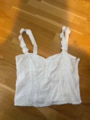 Vit broderad linnetopp med detaljer - Söt vit linnetopp med broderade blommor och  axelband dekorerade med tygrosor.