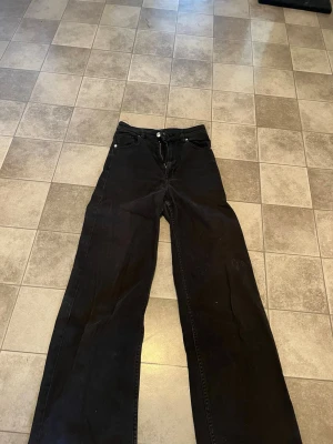 Svarta wide leg jeans från H&M Divided - Svarta jeans med wide leg-modell från H&M Divided. Hög midja och raka, vida ben. Jeansen har knapp- och dragkedjestängning samt bälteshällor. Perfekta för en avslappnad och trendig stil.