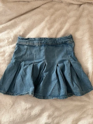 Blå jeanskjol från Pull&Bear - Säljer en blå jeanskjol från Pull&Bear i storlek L. Kjolen har en kort modell med snygga veck och klassisk denimlook. Perfekt för dig som gillar en avslappnad stil till sommaren 💕