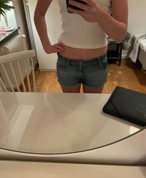 Blå denimshorts från Levi's - Säljer ett par klassiska blå jeansshorts från Levi's med låg midja och femficksmodell. Shortsen har en lågmidja och en normal passform. Slitningarna som är på shortsen var där när de var köpta. På shortsen trå det för 14 år men skulle säga att det är i storlek 32-34 eller xs.  Perfekta till sommaren och lätta att matcha med olika toppar. 💕