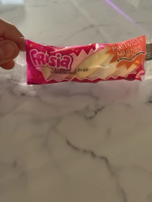 Frisia Mat Twister Mallows godis - En påse Frisia Mat Twister Mallows, ett skruvat marshmallowgodis i rosa, vitt och gult. Förpackningen är färgglad med zigzag-mönster och tydlig logga. Perfekt för dig som gillar sötsaker och vill ha något kul att bjuda på.