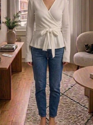 Vit omlottopp med knyt från Aveny - Säljer en vit ribbad omlottopp från Aveny med långa ärmar och snygg knytning i midjan. Toppen har v-ringad hals och sitter riktigt snyggt på kroppen. Perfekt för dig som gillar stilrena och trendiga plagg.