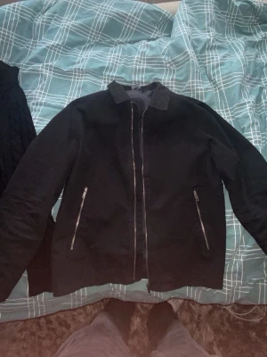 Svart bomberjacka med dragkedjor - Stilren svart bomberjacka med silverfärgade dragkedjor på fickorna och framtill. Klassisk krage och rak passform. Perfekt för dig som vill ha en enkel men snygg jacka till vardagslooken.