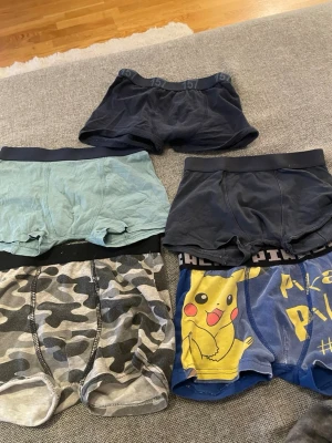 Färgglada kalsonger i olika mönster - Fem par kalsonger i olika färger och mönster, bland annat marinblå, ljusblå, kamouflage och ett par med Pikachu-tryck. Perfekta för dig som gillar variation och bekväma material. Några har bred resår med tryck.