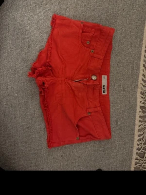 Röda jeansshorts från Moto - Snygga röda jeansshorts från Moto med råa kanter och klassisk femficksdesign. Shortsens material är denim och de har en dragkedja med knapp framtill. Perfekta för sommarens alla äventyr!