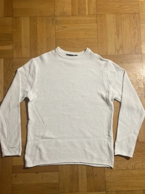 Vit strukturerad långärmad tröja - Säljer en vit långärmad tröja med snyggt strukturerat tyg och rund hals. Tröjan har en enkel och clean look som passar till det mesta. Perfekt för dig som gillar minimalistisk stil.