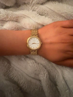 Guldig klocka från Axcent - Stilren klocka från Axcent med rund vit urtavla och guldfärgat metallarmband. Klassisk design med minimalistiska detaljer och länkarmband som ger en lyxig känsla. Perfekt accessoar för dig som gillar eleganta smycken.