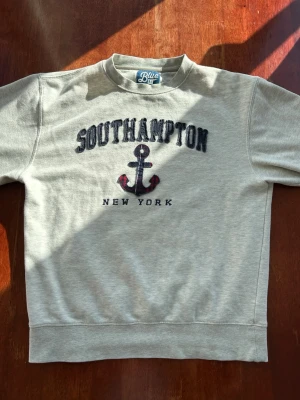Grå sweatshirt med Southampton-tryck - Snygg grå sweatshirt från Blue med texten 'Southampton New York' och ett ankare broderat på bröstet. Tröjan har rund halsringning och är tillverkad i mjukt sweatshirtmaterial. Perfekt för en avslappnad och sportig stil. Gjord av äkta bomull. Riktiga vintage vibbar!