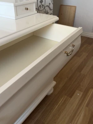 Vit byrå med spegel - Säljer en klassisk vit byrå med oval spegel och tre stora lådor samt två små lådor upptill. Byrån har eleganta guldfärgade handtag och står på rundade ben. Perfekt för förvaring av smink, smycken eller kläder.