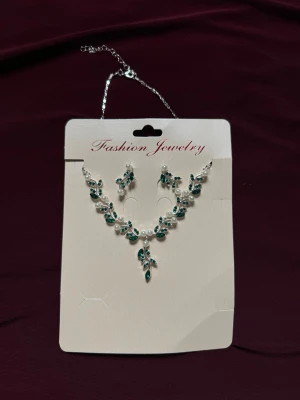 Set med halsband och örhängen, grönt & pärlor - Snyggt smyckeset med halsband och matchande örhängen. Setet har silverfärgad kedja, gröna bladformade detaljer och vita pärlor som ger en elegant look. Perfekt för att lyfta din outfit med lite extra bling.