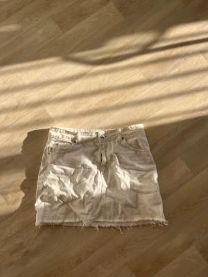 Vit jeanskjol från Topshop Moto - Säljer en vit jeanskjol från Topshop Moto med rå kant nertill och klassisk femficksdesign. Kjolen har dragkedja och knapp framtill och är i en kort modell. Perfekt för dig som gillar en enkel men snygg stil.