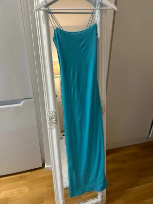 Turkos ribbad långklänning - Säljer en turkos ribbad långklänning med tunna axelband och figurnära passform. Köpt i Marocko. Klänningen har en enkel och stilren design som passar perfekt till sommaren. Materialet känns mjukt och stretchigt för en bekväm känsla.
