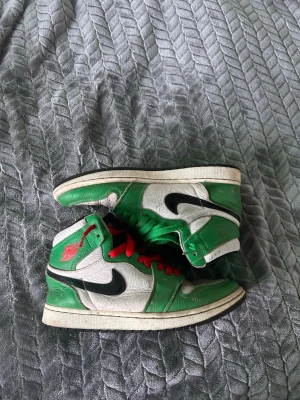 Nike Air Jordan 1 Retro High Grön/Vit - Snygga Nike Air Jordan 1 Retro High sneakers i grönt och vitt med svarta swoosh-detaljer och kontrasterande röda och gröna skosnören. Klassisk high-top siluett med läderöverdel och ikonisk Air Jordan-logga på sidan.