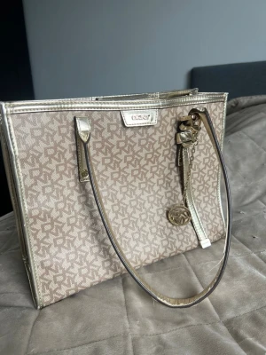 Vintage bag from DKNY - This beige rare  tote bag from DKNY features the signature logo print and gold-tone trim